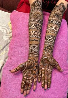 two hands with henna tattoos sitting on top of a pink blanket in front of a bed