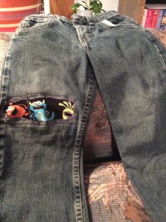 an old pair of jeans with embroidered monsters on the back and side pockets, sitting on a couch