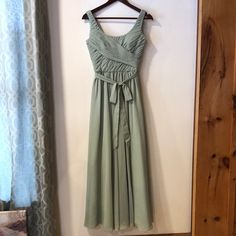 a green dress hanging on a wall in front of a door with a wooden hanger