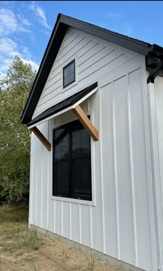 a small white house with a black roof and window trims on the side of it