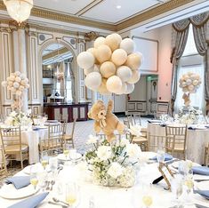 a teddy bear is on top of a table with white flowers and balloons in the air