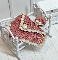 a crocheted blanket and hat are on a doll's bed with white rails