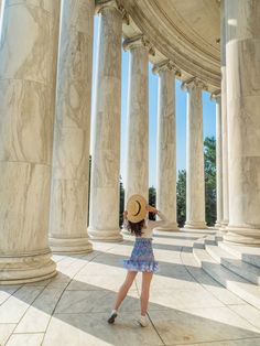 a woman standing in front of columns with a hat on her head looking up at the sky