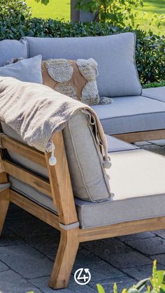 a couch with pillows on it sitting in the middle of a patio next to some bushes