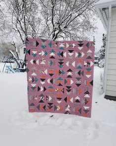 a pink quilt sitting on top of snow covered ground next to a tree and house