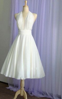 a white dress on a mannequin stand in front of purple curtained background