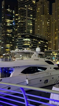 several yachts are docked in the harbor at night with skyscrapers in the background