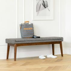 a bench with a bag and shoes on it in front of a white wall next to a wooden floor