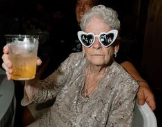 an older woman wearing sunglasses holding up a beer