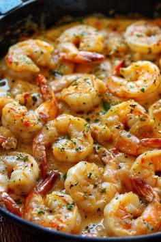 a pan filled with shrimp and sauce on top of a wooden table