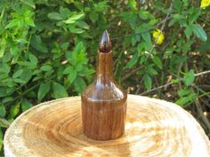 a small wooden bottle sitting on top of a tree stump in front of some bushes