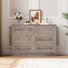 a dresser with flowers and pictures on it in a white walled living room, next to a potted plant