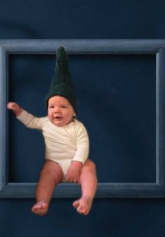 a baby wearing a green hat sitting in front of a blue framed photo with one foot on the ground