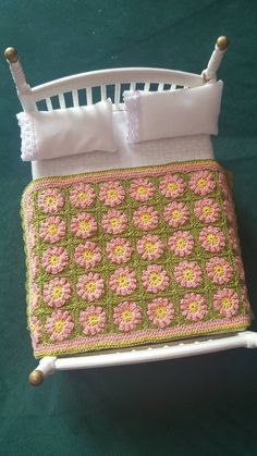 a crocheted blanket is on top of a doll's bed with a white headboard and foot board