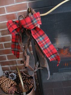 a red and black plaid bow is hanging on a fireplace mantel with pine cones