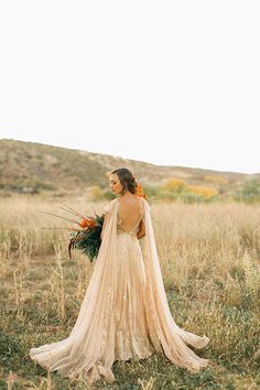 a woman in a wedding dress standing in a field with her back to the camera