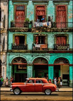 an old red car is parked in front of a blue building with balconies