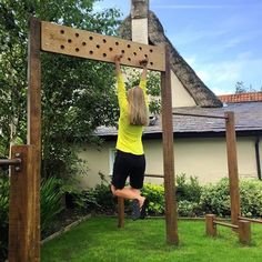 a woman is hanging on to a wooden structure in the grass with her hands up