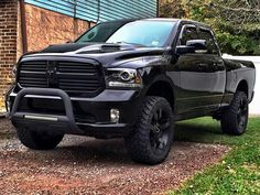 a black dodge ram truck parked in front of a brick building with green grass and trees