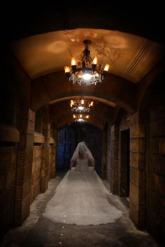 the bride is walking down the aisle in her wedding dress and veil with chandelier