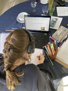 a woman wearing headphones sitting at a table with books and notebooks in front of her