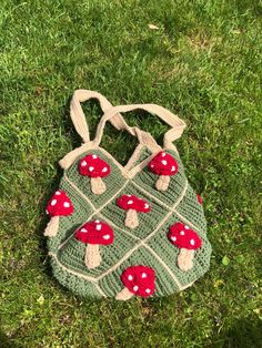 a crocheted bag with red mushrooms on it sitting in the grass next to some green grass