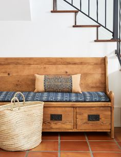 a wooden bench sitting next to a basket on top of a tiled floor in front of a stair case