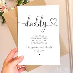 a hand holding up a card with the words daddy written on it and flowers in the background