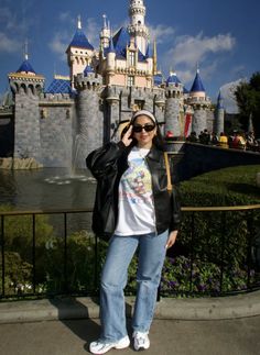 a woman standing in front of a castle wearing sunglasses and a black jacket with mickey mouse on it