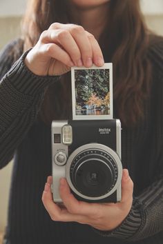 a woman holding up a polaroid camera in front of her face and taking a picture