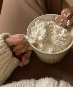 a person holding a cup with whipped cream and a gingerbread cookie in it on their lap