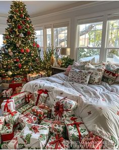 a bed covered in lots of presents under a christmas tree next to a large window