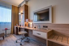 a hotel room with a desk, chair and television on the wall in front of a large window