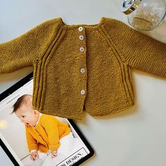 a baby's sweater and magazine sitting on a table next to a glass of water