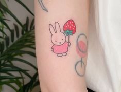 a person with a tattoo on their arm holding a red mushroom and bunny in her hand