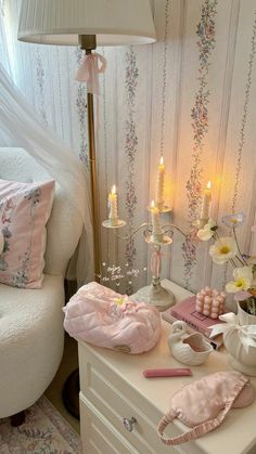 a white dresser topped with lots of items next to a lamp and bed covered in pink sheets