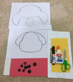 paper cut outs with scissors, glue and buttons on the floor next to it is a drawing of a person wearing a hat