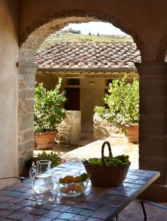 an outdoor table with two baskets and wine glasses on it in front of a stone archway