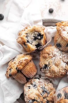 several blueberry muffins on a plate with powdered sugar and blackberries