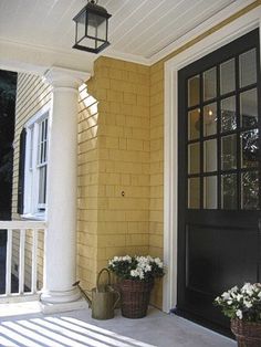 two flower pots are sitting on the front porch next to a black door and light fixture