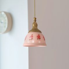 a pink lamp hanging from the ceiling next to a wall with a clock on it