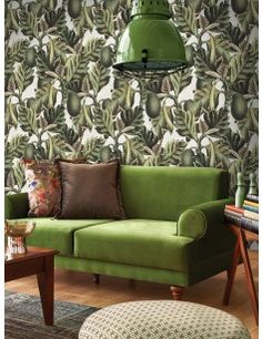 a green couch sitting in front of a wallpapered with leaves and plants on it