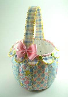 a blue and white flowered basket with a pink bow on the front, sitting on a table