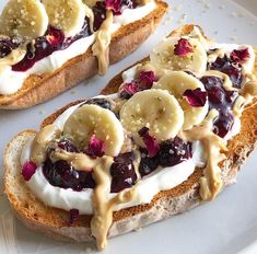 two pieces of bread with bananas and blueberry toppings on them sitting on a white plate