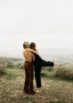 two women standing on top of a grass covered field next to each other with their arms around one another