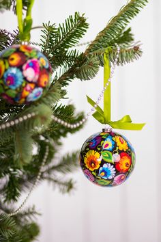 three ornaments hanging from a christmas tree with green branches and white wall in the background