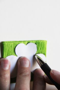 a person is holding a pen and cutting out a piece of paper that looks like a clover