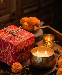 a candle is lit next to a red box and some flowers on a wooden table