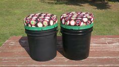 two black trash cans sitting on top of a wooden table next to green trimming