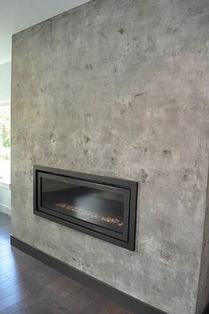 a fire place in the middle of a room with wood flooring and concrete walls